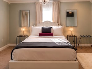 Une chambre à coucher avec un lit, deux tables de chevet, un lustre et un grand miroir.
