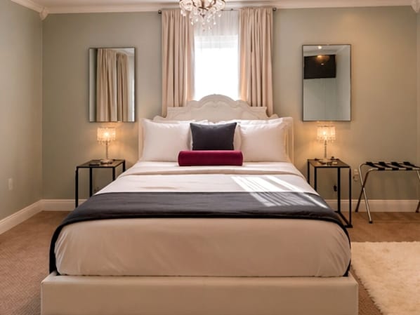 A bedroom with a bed, two bedside tables, a chandelier, and a large mirror.