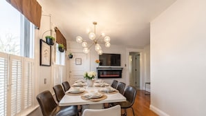 Una sala da pranzo con un tavolo bianco imbandito per sei persone, circondato da poltrone in pelle, un lampadario e un camino.