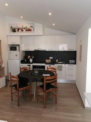 Une cuisine compacte avec des meubles blancs, un plan de travail noir et une table à manger entourée de quatre chaises en bois.