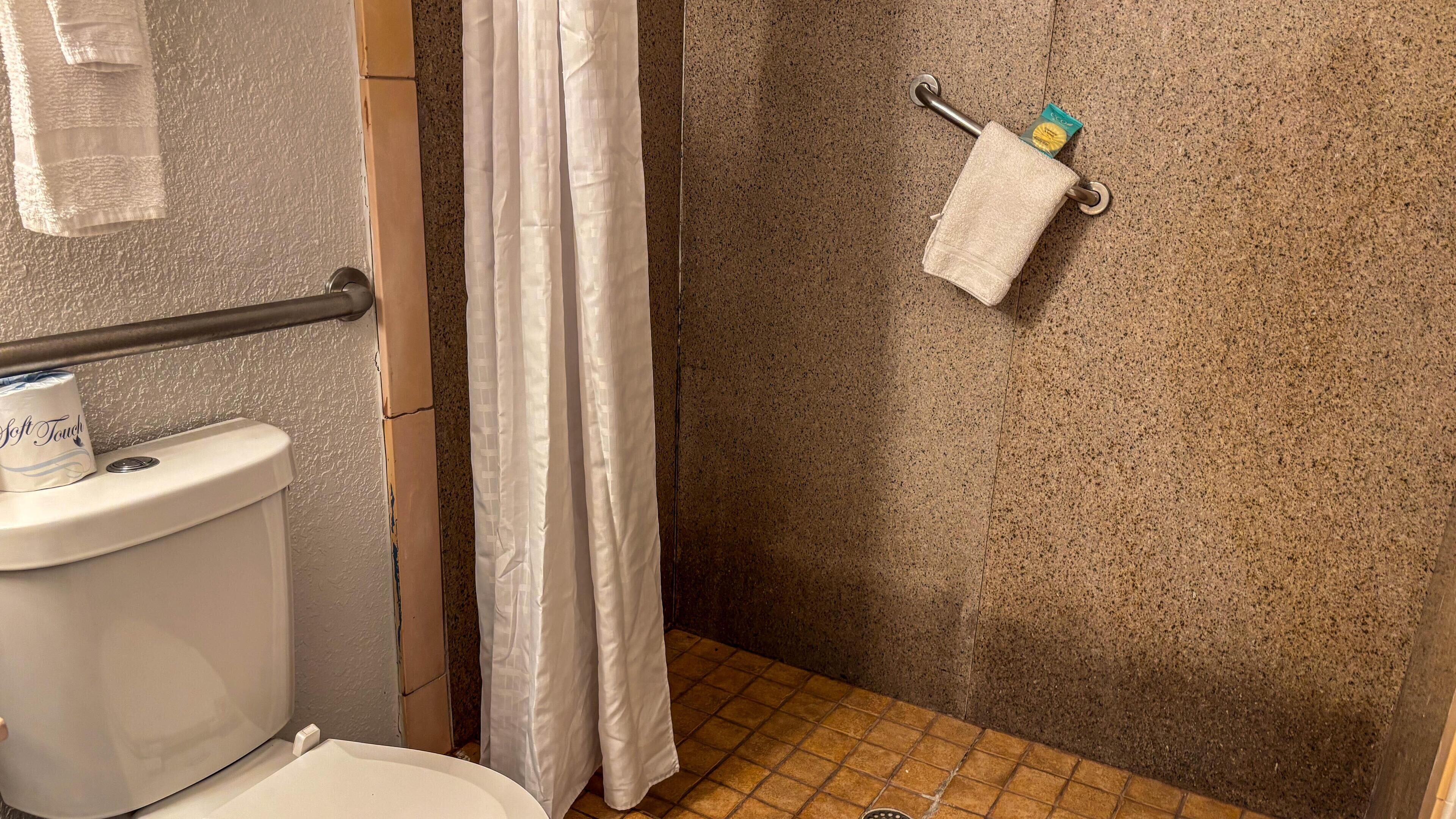 Ein Badezimmer mit Dusche, Toilette und Handtuchhalter mit Handtuch und einer kleinen Flasche.