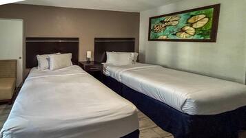 A hotel room with two single beds, a nightstand, a lamp, and a painting on the wall.