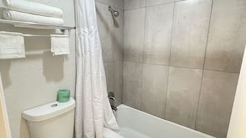 A bathroom with a toilet, bathtub, and shower. There are towels on a rack and a toilet paper holder.