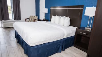 A hotel room with a large bed, a chair, a desk, and a window with curtains.