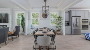 A spacious kitchen with modern appliances, a dining area with a wooden table and chairs, and large windows offering a view of the outdoors. - 17 Modern Beach Getaway w/ Tesla Charger, Fire Pit  & Games (Hilton Head Island)