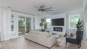 A modern living room with a large sectional sofa, a grey armchair, a flat-screen TV, and a fireplace. - 17 Modern Beach Getaway w/ Tesla Charger, Fire Pit  & Games (Hilton Head Island)