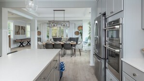 A modern kitchen with stainless steel appliances, a dining area with a table and chairs, and a large island with a sink. - 17 Modern Beach Getaway w/ Tesla Charger, Fire Pit  & Games (Hilton Head Island)