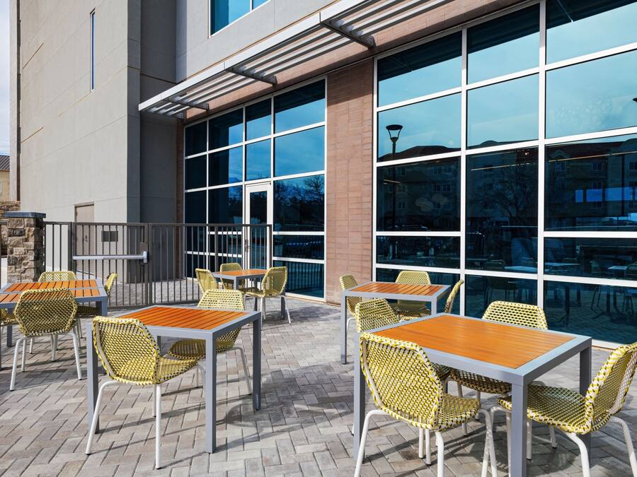 An outdoor patio area with tables and chairs, large windows, and a brick wall.