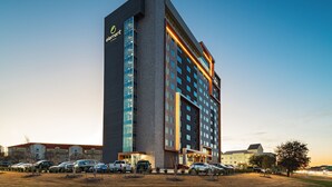 A modern hotel with a prominent vertical sign, multiple floors, and a parking lot with several cars. - Element by Marriott Dallas Las Colinas (Irving)