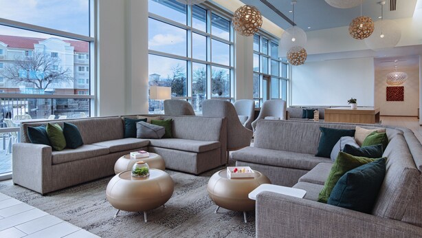A modern living room with large windows, grey sofas, round coffee tables, and decorative lighting. - Element by Marriott Dallas Las Colinas (Irving)