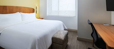 A hotel room with a bed, a wooden headboard, a window with a view, a desk, and a chair.