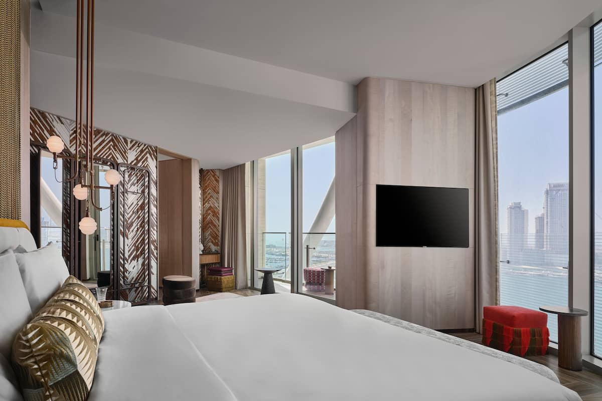 Une chambre d’hôtel moderne dotée d’un grand lit, d’un téléviseur à écran plat fixé au mur et d’un balcon offrant une vue sur la ville.