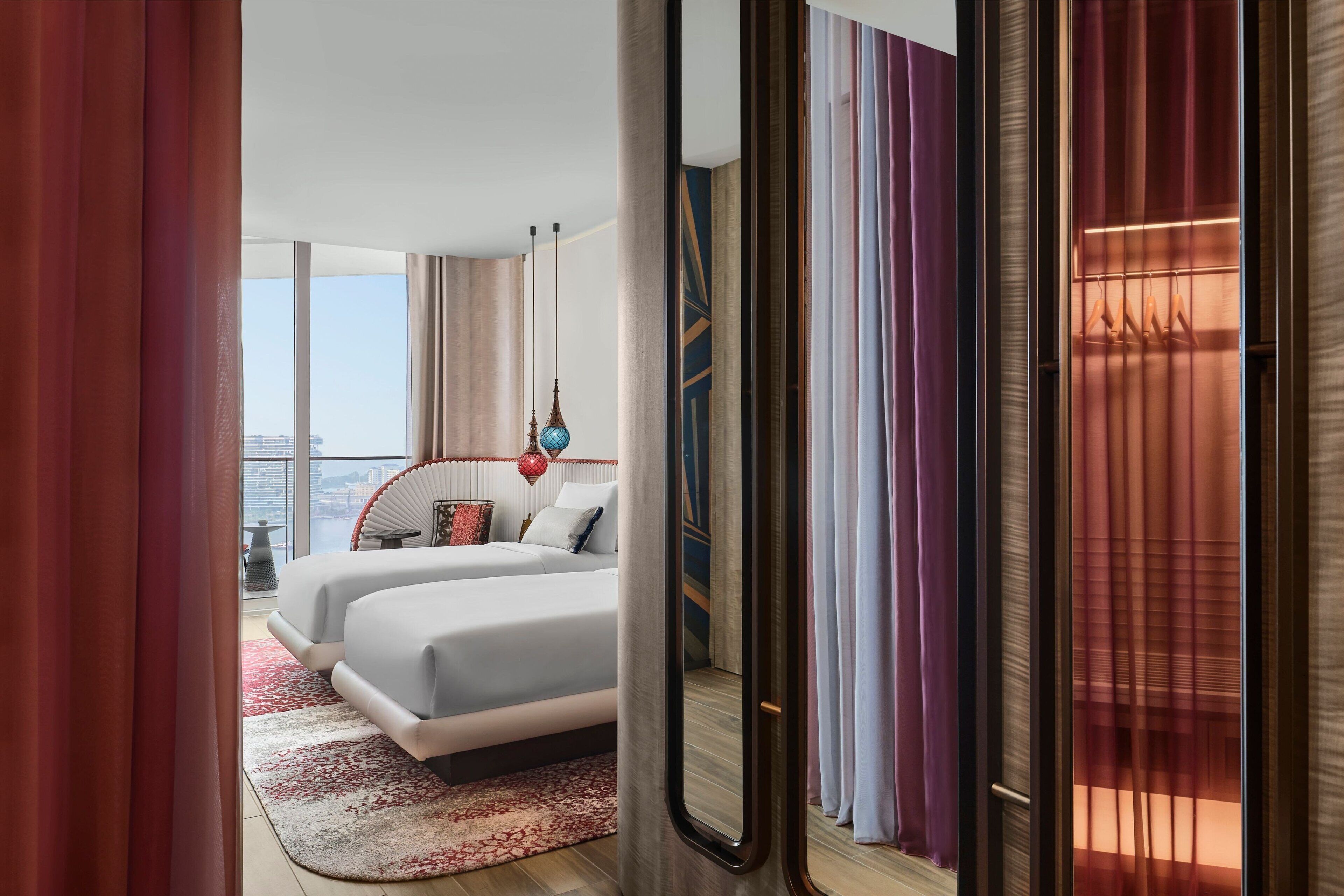 A modern hotel room with a large bed, a view of the city, and a balcony with curtains.