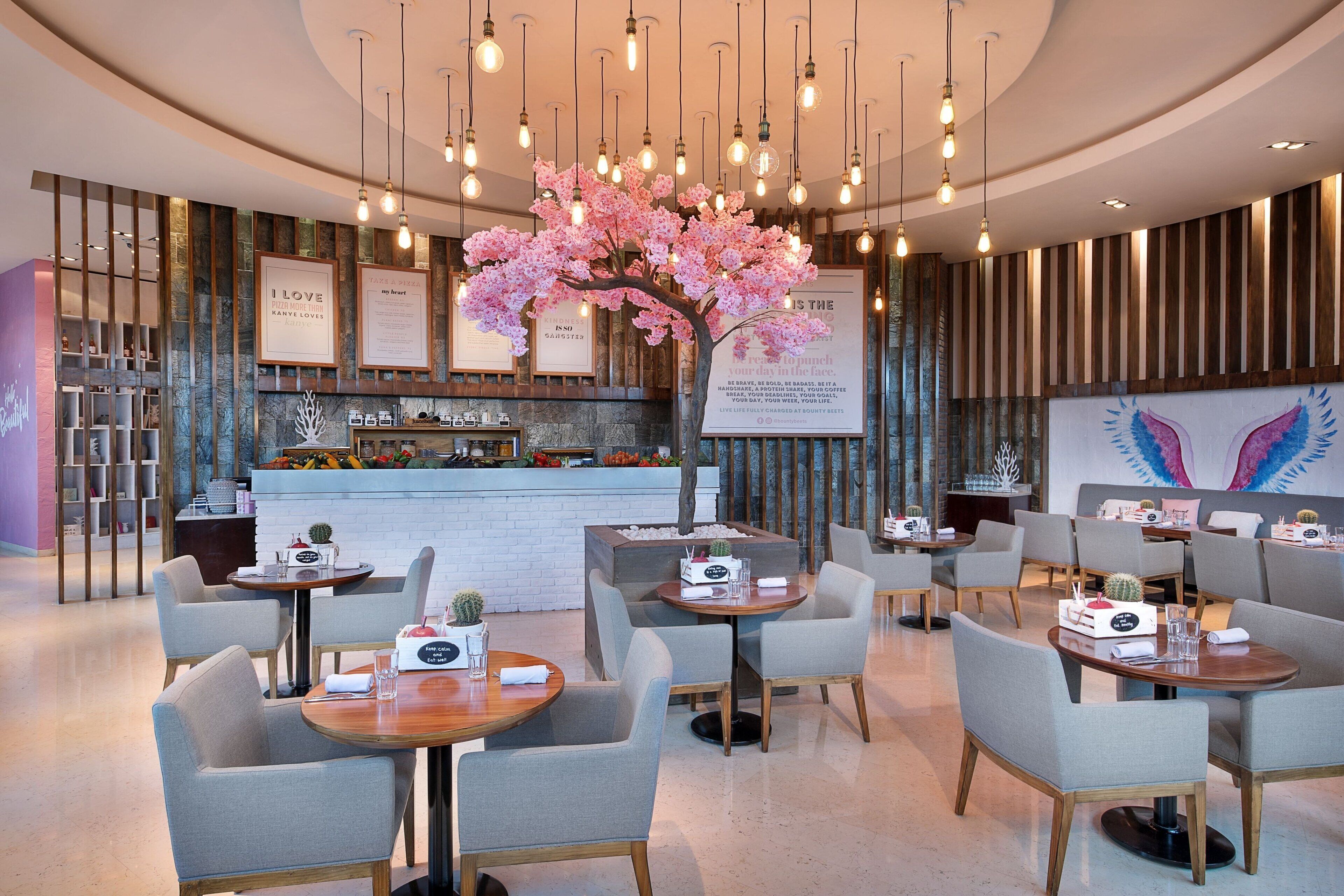 Un restaurant moderne avec des tables et des chaises rondes, un arrangement floral central et un bar situé au fond de la salle.