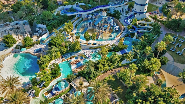 An aerial view of a resort with multiple swimming pools, water slides, and a lighthouse tower.