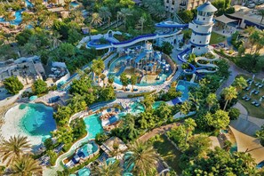 An aerial view of a resort with multiple swimming pools, water slides, and a lighthouse tower.