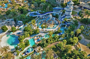 Vista aérea de un resort con múltiples piscinas, toboganes de agua y una torre de faro.