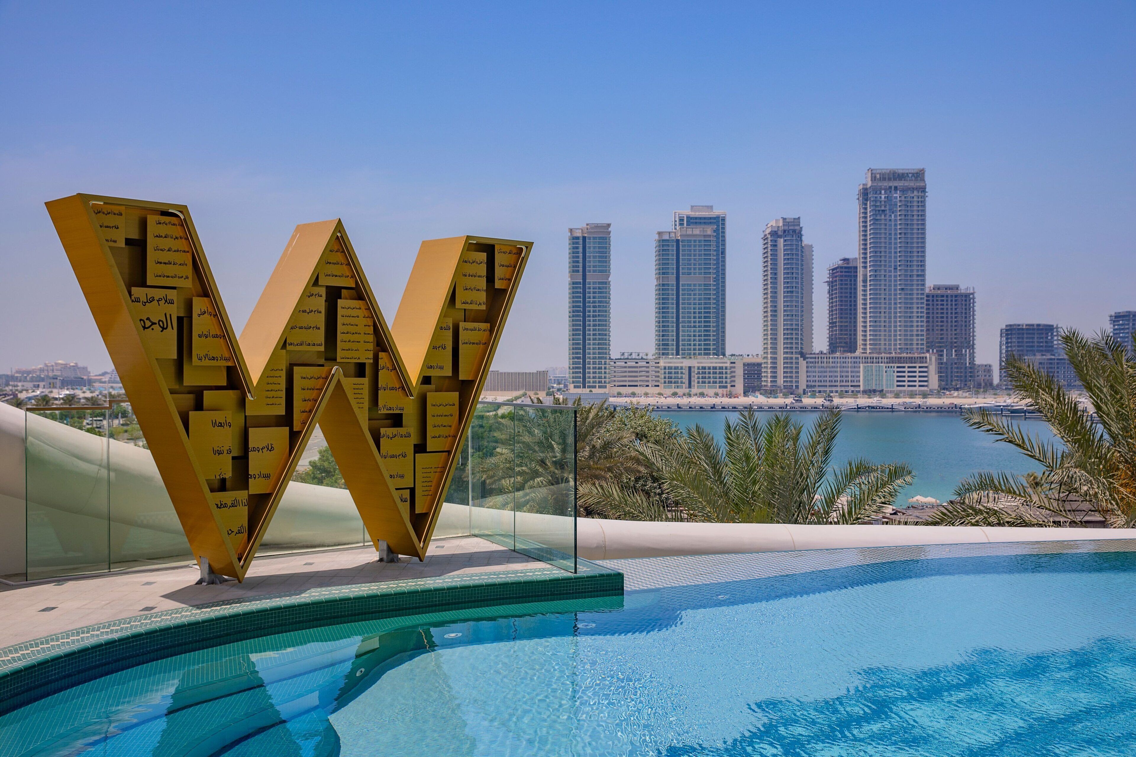 A modern pool area with a large golden 'W' structure and a city skyline in the background.
