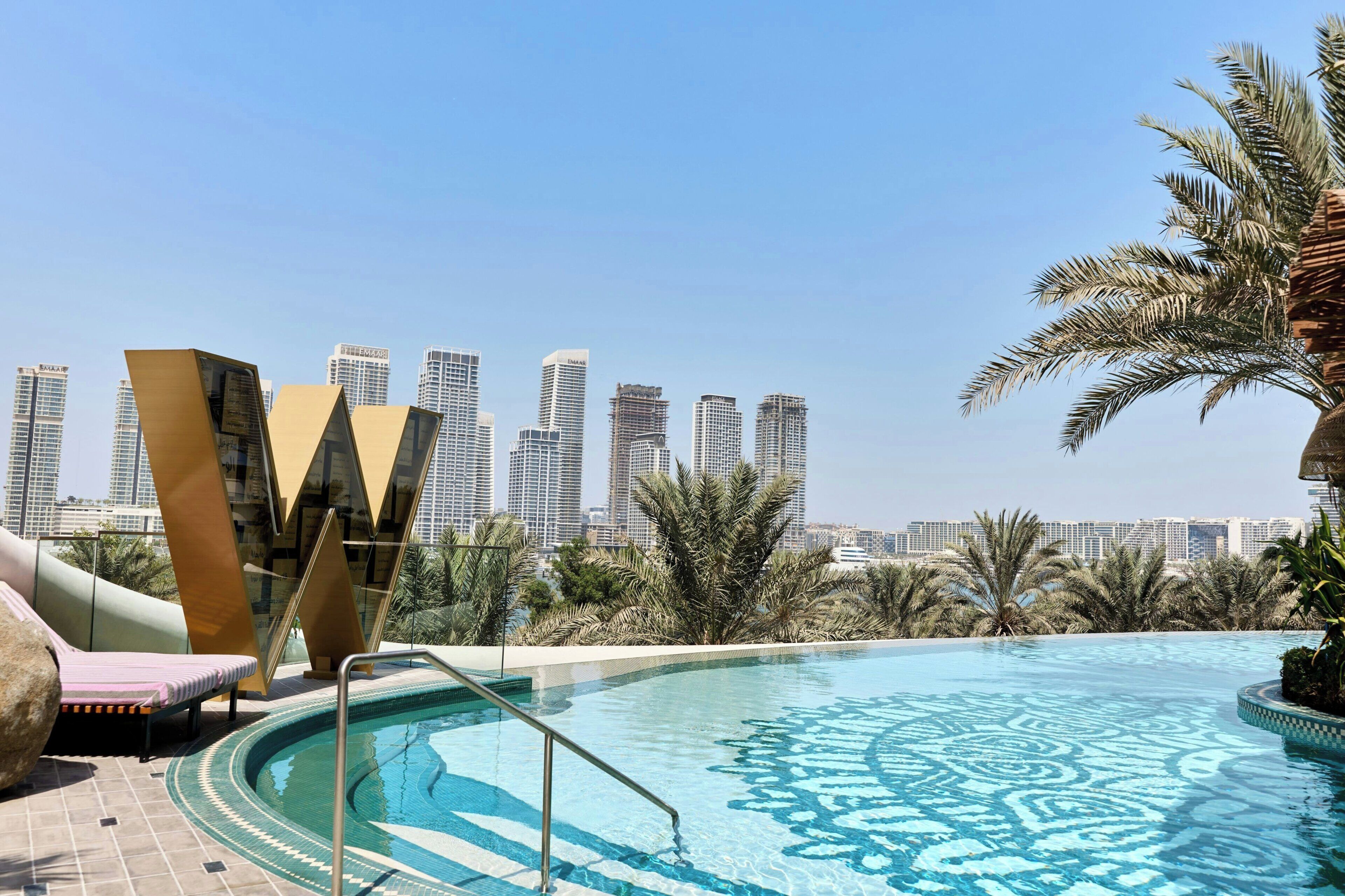 A rooftop pool with a city skyline in the background, palm trees, and modern buildings.