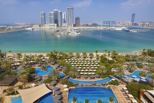 Un resort con varias piscinas, palmeras y un puerto deportivo con barcos.