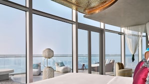 A high-rise hotel room with a large bed, a view of the cityscape, and a balcony with seating.