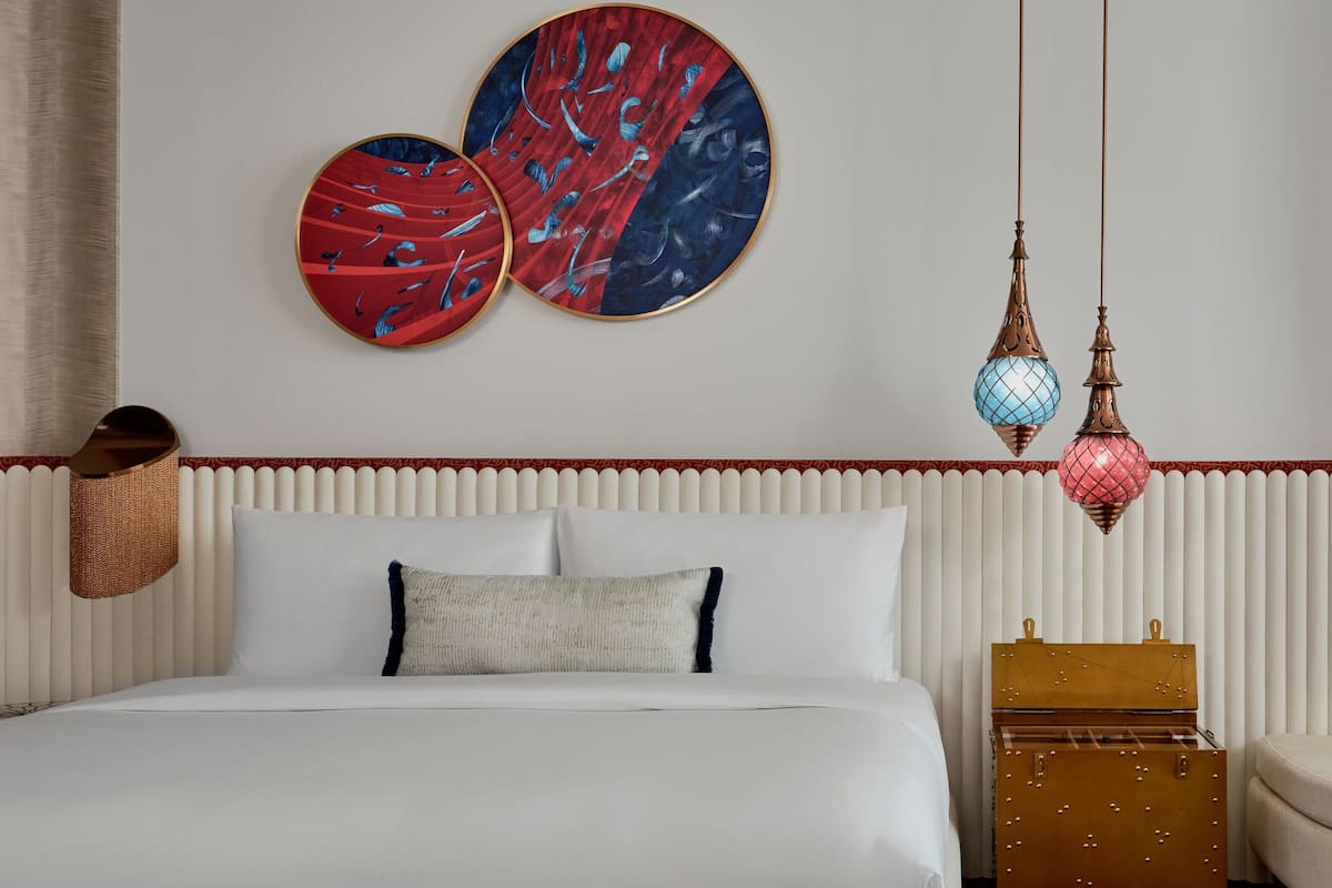 Un lit bien fait, avec du linge de lit blanc, un panier en osier et une décoration murale.
