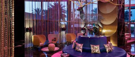 A modern lounge area with a blue sofa, pink and gold accents, and a decorative tree sculpture.