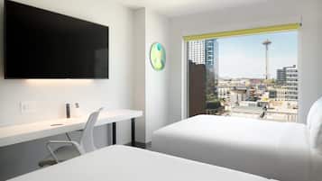 A modern hotel room with a bed, a desk, a chair, a flat-screen TV, and a window with a city view.