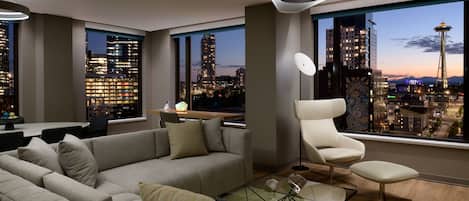 Un salón moderno con un sofá grande, una mesa de centro de vidrio y vistas a un paisaje urbano que incluye una torre destacada.
