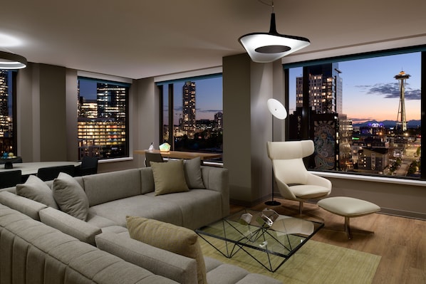 Un salón moderno con un sofá grande, una mesa de centro de vidrio y vistas a un paisaje urbano que incluye una torre destacada.