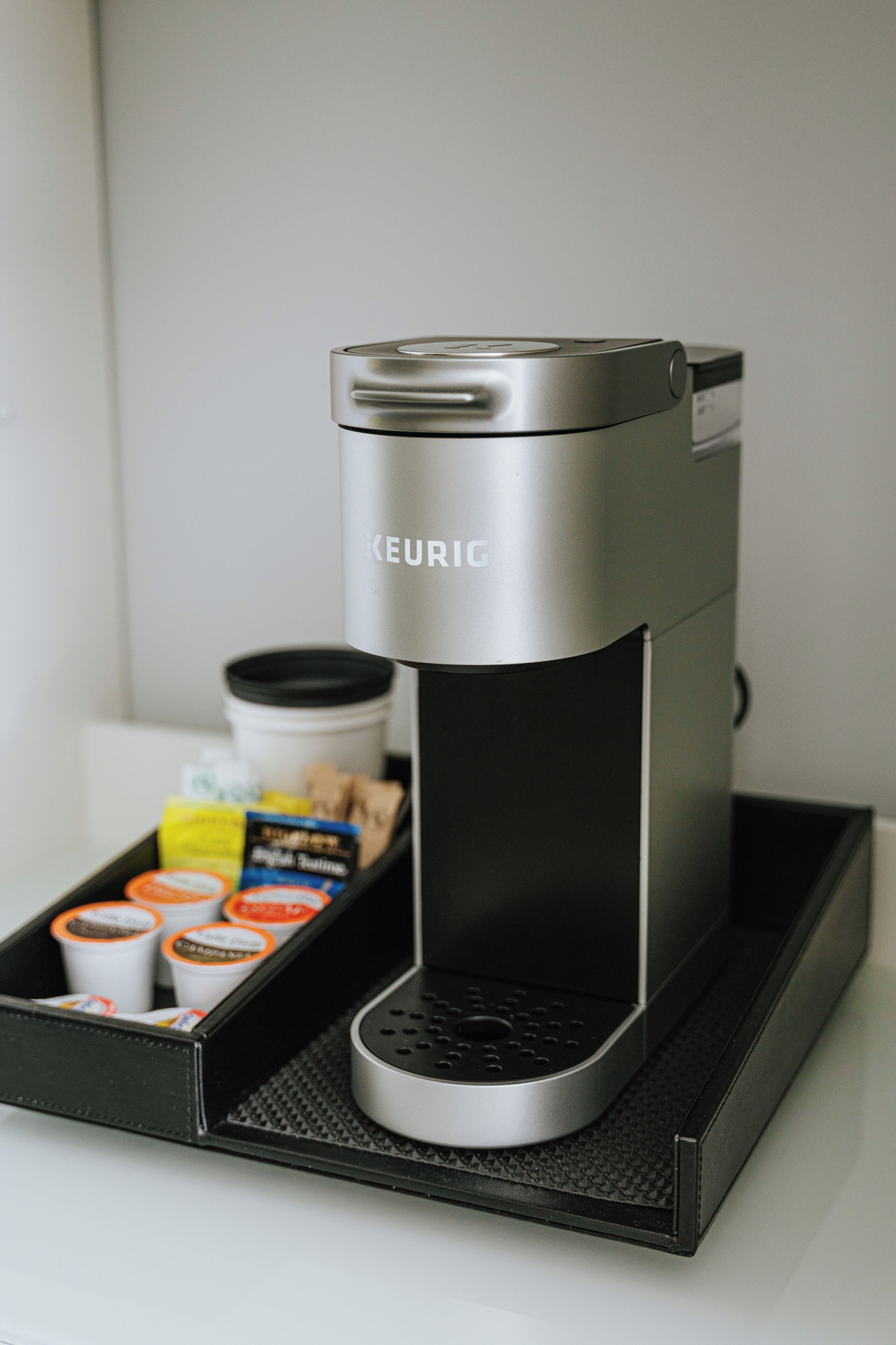 Una cafetera Keurig con un recipiente para goteo, cápsulas de café y depósito de agua.
