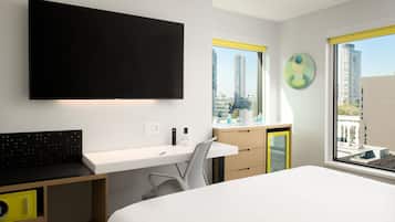 Une chambre d’hôtel moderne dotée d’un grand lit, d’un bureau avec une chaise, d’un téléviseur à écran plat fixé au mur et d’une fenêtre donnant sur la ville.