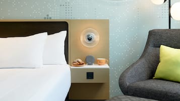 Una habitación de hotel con una cama bien hecha, una mesita de noche con una lámpara, una taza y un pastel.