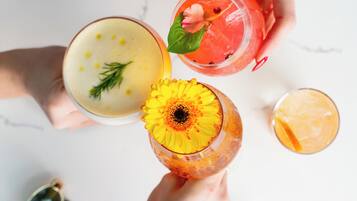 Von oben betrachtet, ein weißer Tisch mit verschiedenen Getränken, darunter eine Ananas-Garnitur und eine Blume, sowie ein Paar Sonnenbrillen.