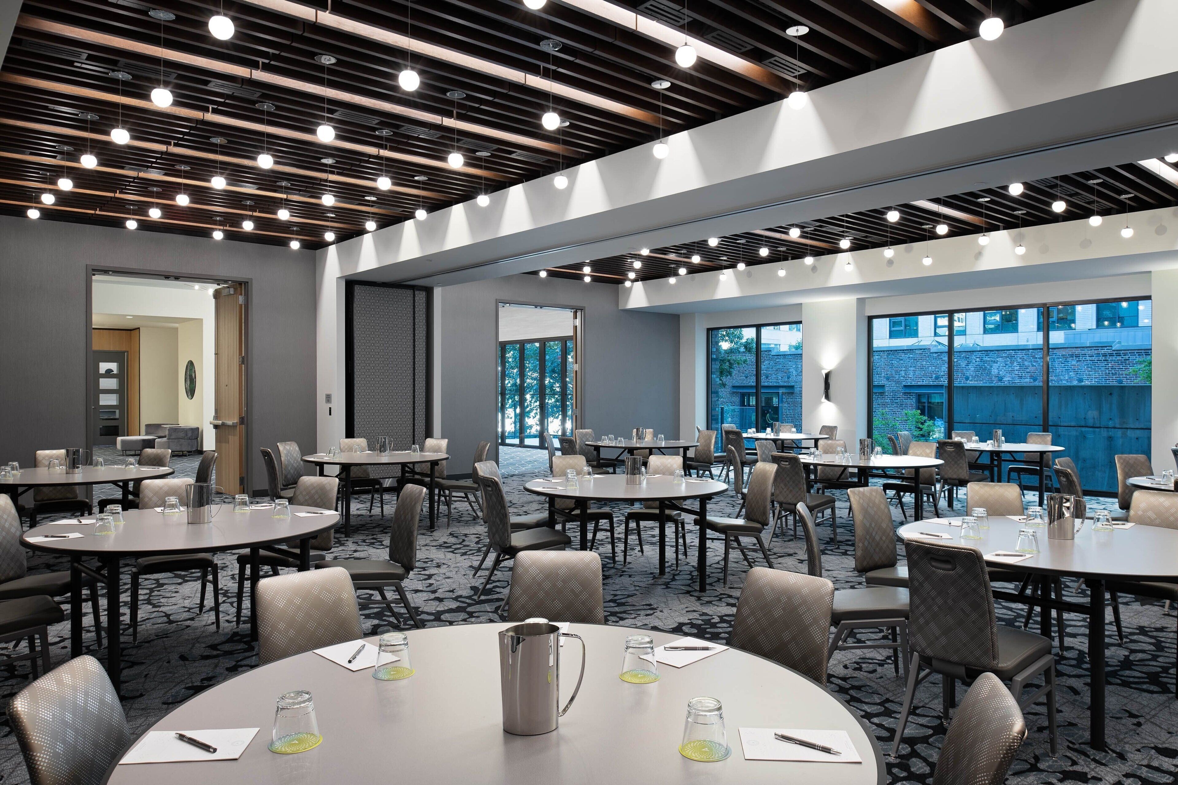 A modern conference room with round tables, chairs, and a ceiling with exposed beams and lighting fixtures.