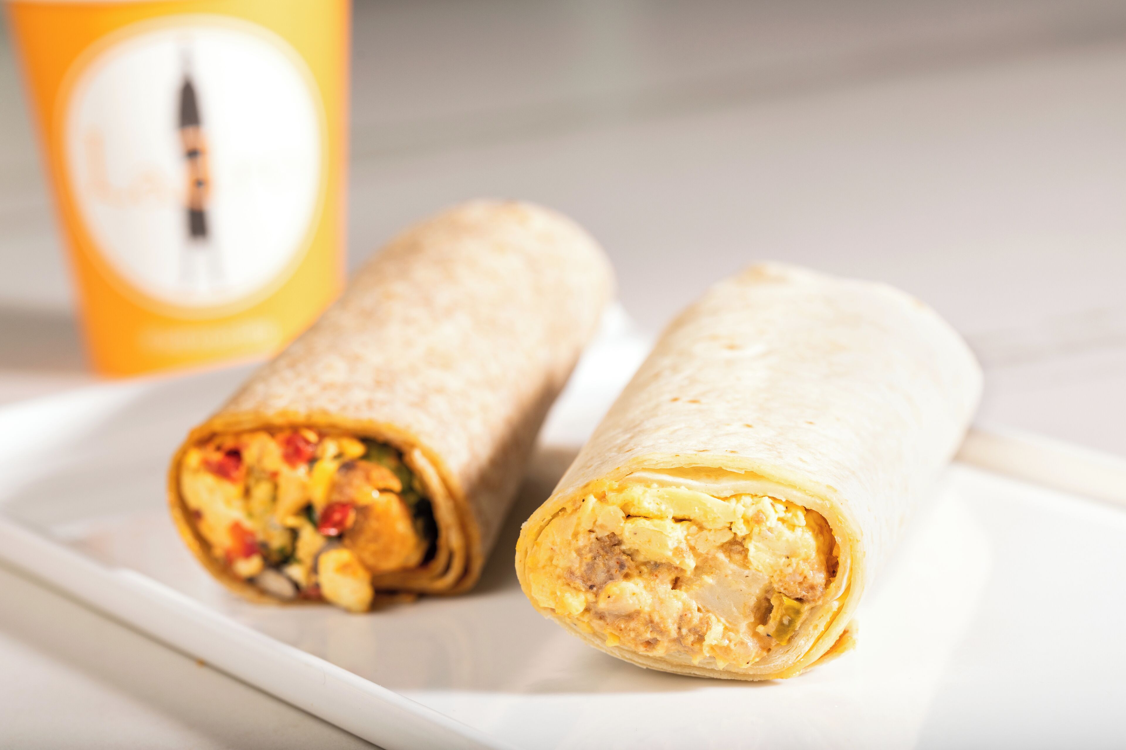 Two burritos on a white plate with a blurred background.