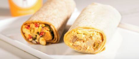 Two burritos on a white plate with a blurred background.