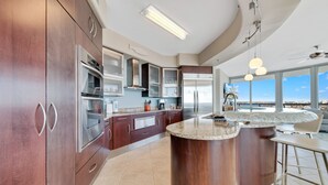 A modern kitchen with stainless steel appliances, wooden cabinets, and a large island. - Bella Luna 810-Spectacular Views of Beach & Bay (Orange)