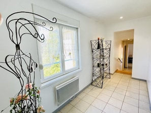 Une pièce avec un radiateur, une fenêtre avec des rideaux, une sculpture métallique décorative et un sol carrelé.