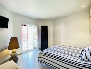 A bedroom with a bed, a lamp, a TV, and a sliding door to a balcony.