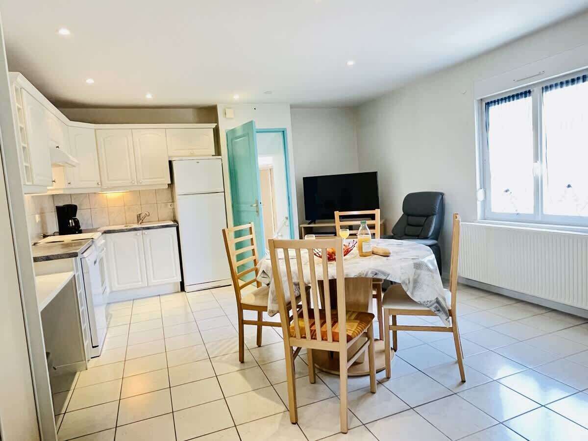 Une cuisine moderne avec des meubles blancs, une table à manger avec des chaises, un téléviseur et une fenêtre avec des rideaux.