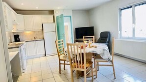 A modern kitchen with white cabinets, a dining table with chairs, a TV, and a window with curtains. - Bonaparte (Bains-les-Bains)