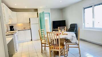 Une cuisine moderne avec des meubles blancs, une table à manger avec des chaises, un téléviseur et une fenêtre avec des rideaux.