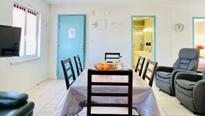 Un comedor con una mesa dispuesta para dos personas, sillas, un televisor y una puerta que da a un baño.