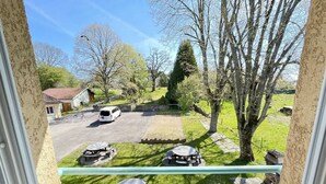 Vista desde una ventana que da a un estacionamiento con varios coches, mesas al aire libre y árboles.