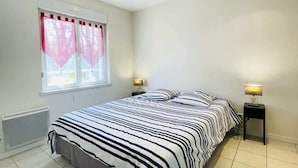 Un dormitorio con cama, dos mesitas de noche, una ventana con cortinas y un radiador.