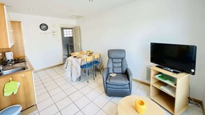 A compact living space with a kitchenette, a dining area, a seating area with a TV, and a small table. - Victor Hugo (Bains-les-Bains)