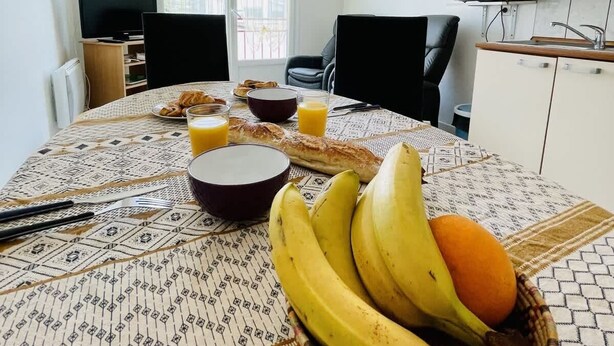 A dining table with breakfast items, a television, and a kitchen area with cabinets and a microwave. - Victor Hugo (Bains-les-Bains)