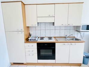 A compact kitchen with white cabinets, a stove, oven, and a sink.