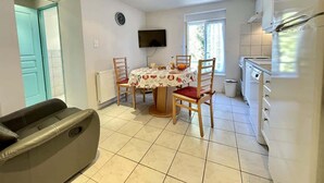 Un comedor con mesa, sillas, televisor y zona de cocina con refrigerador.